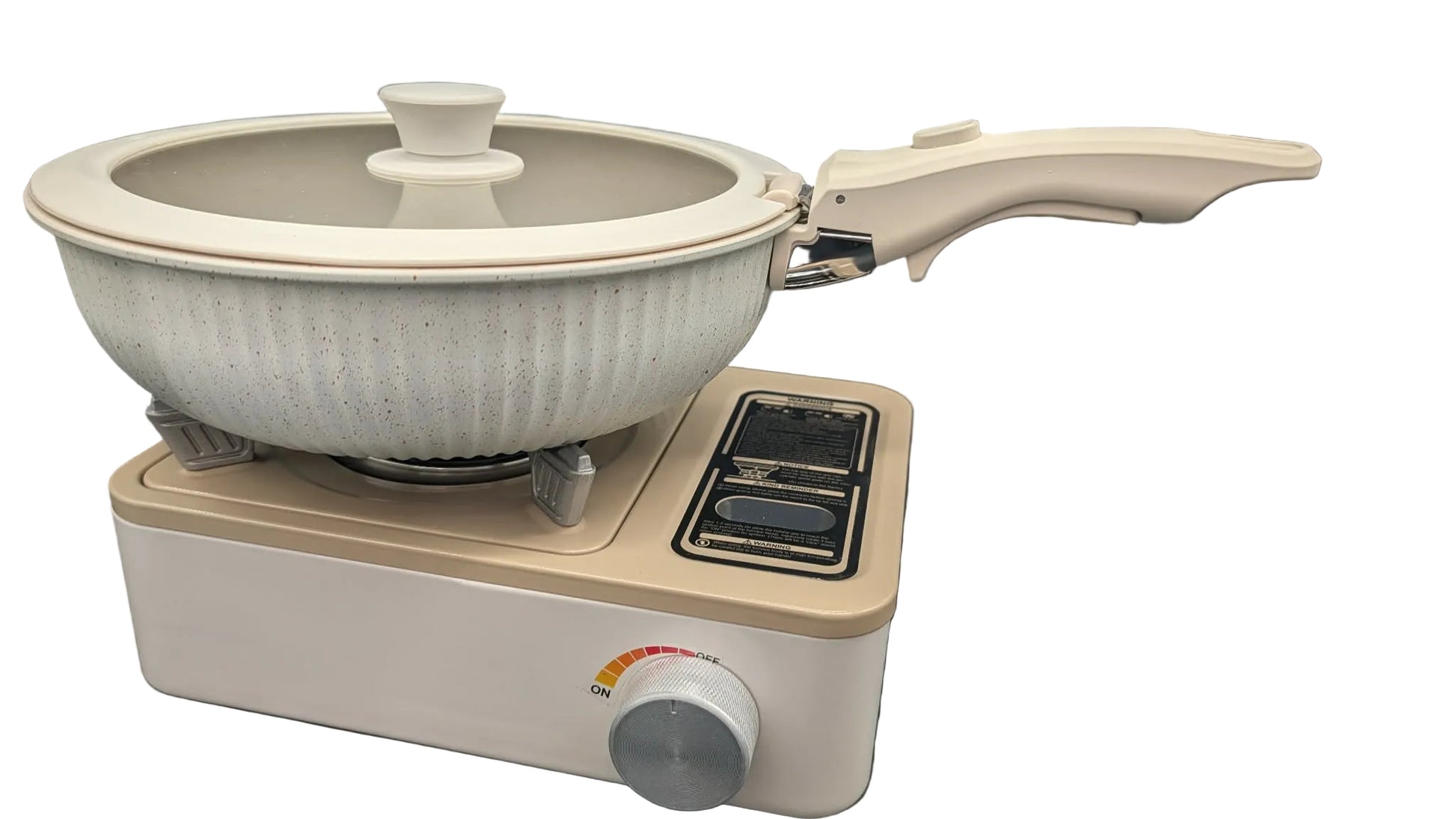 A ceramic non-stick pan with a matching lid sits on a compact portable electric burner. The pan has a ribbed off-white exterior and a cream-colored handle, while the burner is beige with a black control panel and a silver dial, set against a dark gray background.